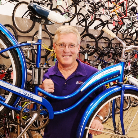 Business photography editorial of a male professional in a purple shirt at a bike shop holding a blue bike.